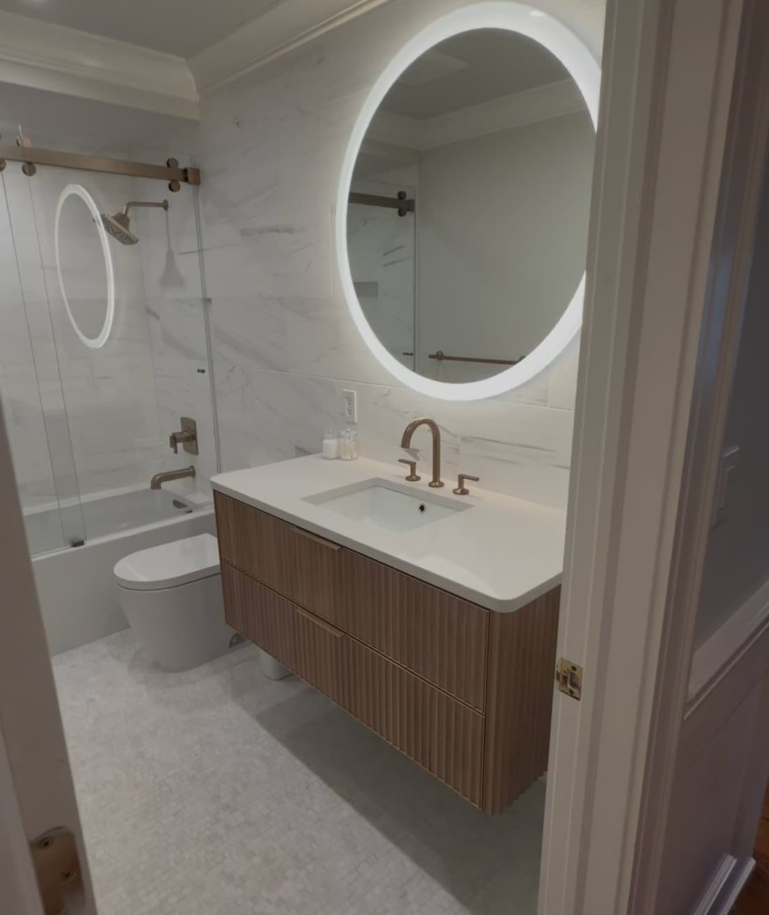 Guest bathroom with round LED mirror, floating vanity and marble tile